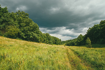 Obraz premium Picturesque and winding hills with fields, roads and dramatic pre-storm skies