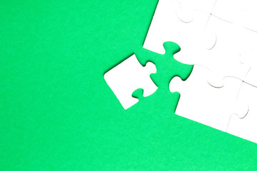 unfinished puzzle made of white cardboard on a green background and one unsuitable part from another puzzle, one piece is missing, copy space, search for some suitable part, team building concept