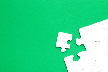 unfinished puzzle made of white cardboard on a green background and one unsuitable part from another puzzle, one piece is missing, copy space, search for some suitable part, team building concept