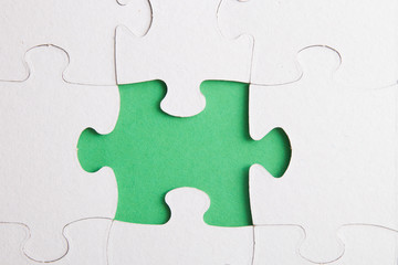 Fototapeta premium unfinished puzzle made of white cardboard on a green background and one unsuitable part from another puzzle, one piece is missing, copy space