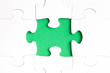 unfinished puzzle made of white cardboard on a green background and one unsuitable part from another puzzle, one piece is missing, copy space