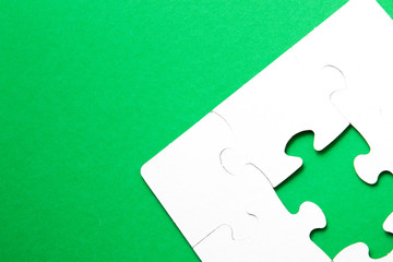 unfinished puzzle made of white cardboard on a green background and one unsuitable part from...