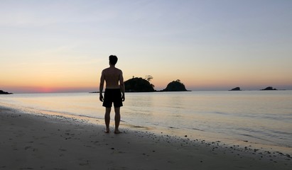 Naklejka premium Silhouette of man standing at Nacpan beach during sunset , before small island, El Nido, Palawan, Philippines