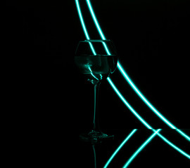 Cocktail in a glass wine glass with neon mint stripes on a black background. Close up