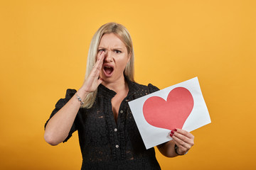 Beautiful blonde girl in black dress on yellow background an irritated angry woman screams...