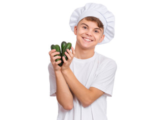 Happy teen boy in chef hat holding fresh green cucumbers, isolated on white background. Portrait of smiling child cook shows delicious raw vegetables in hands. Organic natural healthy food produce.