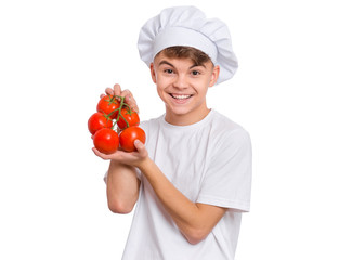 Happy teen boy in chef hat holding fresh red tomatoes branch, isolated on white background. Portrait of cute smiling child shows delicious raw vegetables in hands. Organic natural healthy food produce