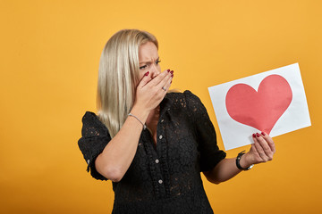 Beautiful blonde girl in black dress on yellow background shocked nervous irritated woman put hand...
