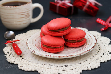 Red macaroons and cup of coffee are located on a plate on a dark background