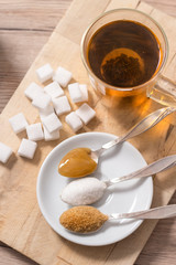 Różne rodzaje cukru leżą na drewnianej desce. Herbata zaparzona w szklance.  - obrazy, fototapety, plakaty