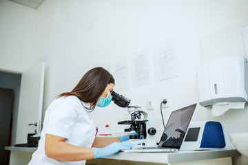 Charming caucasian laboratory assistant in white uniform, with protective mask and rubber gloves...