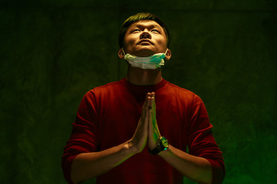 Asian man with protective nask looking up and praying to God