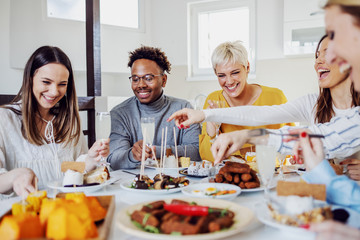 Group of happy multicultural friends sitting at dinning table and having lunch at home.