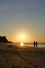 Fototapeta na wymiar Sunset with orange sky at Nacpan beach with two girls and sitting dog, El Nido, Palawan, Philippines