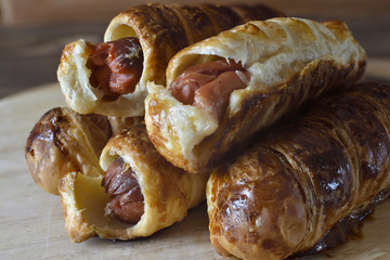 Sausages baked in dough on a wooden tray.