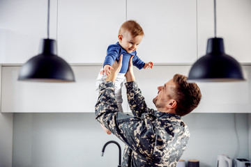 Young soldier just arrived home and he is so happy to see his son. Man is lifting toddler.