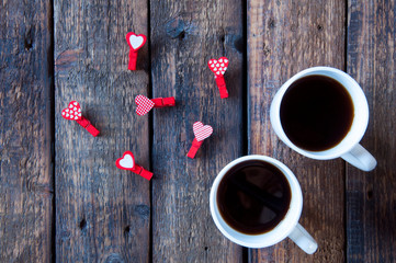 Two white cups with tea or coffee on a wooden background. Little red clothespins hearts