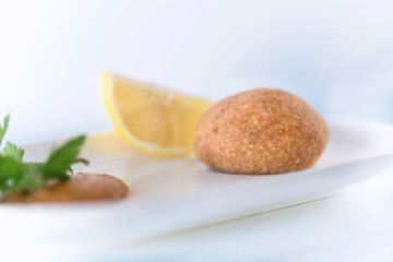 Boiled stuffed meatballs preapred with cracked wheat,  minced meat and spices with pepper sauce and a half lemon on a white background, close up