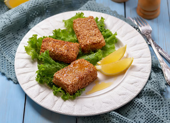 Pan fried feta with honey and sesame seeds served with lemon wedges on white plate. Greek appetizer Feta saganaki.