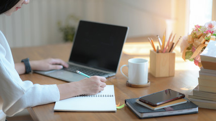 Young businesswomen are taking notes and using a blank screen laptop in a modern office.
