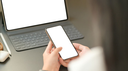 Obraz premium Close up image of the hand of a businesswoman is using a blank screen smartphone with a laptop.