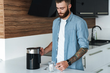 Smiling young bearded man making cup of tea