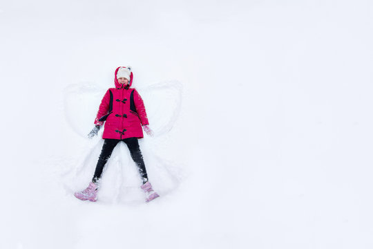 girl lies in the snow and makes an asterisk