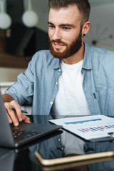 Smiling young bearded man working on laptop computer