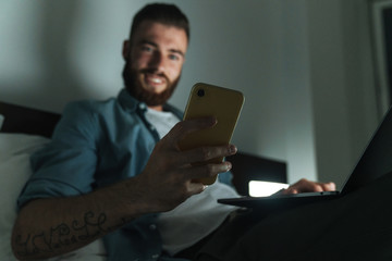 Smiling young bearded man laying on bed at home