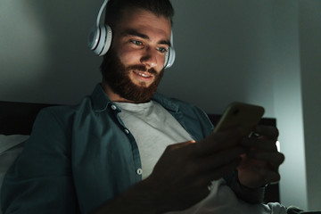 Smiling young bearded man laying on bed at home