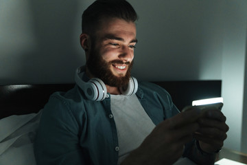 Smiling young bearded man laying on bed at home