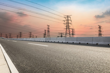High voltage power tower and empty asphalt road at dusk