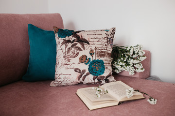 close up photo of two pillows on the sofa in the room. Open book and flowers in the frame.