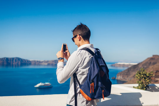 Santorini traveler man taking photo of Caldera from Fira, Greece on phone. Tourism, traveling, vacation concept