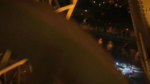 Girders of the Eiffel tower going up the elevator。 Going up the Eiffel tower's elevator, we see the girders passing  by with the city of Paris at night in the background. 