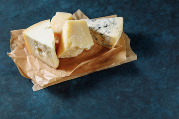 Different sorts of cheese on a parchment paper on dark blue textured background