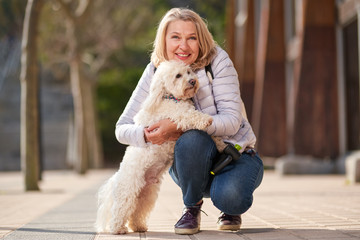 mature woman walking with fluffy white dog in summer city