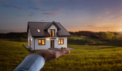 Concept of buying or building new home. Male hand showing, offering a new dream house at the empty field with copy space - obrazy, fototapety, plakaty