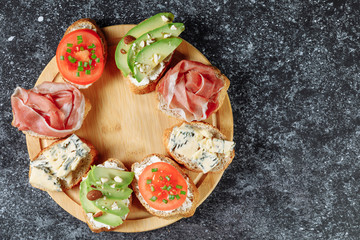Traditional Italian bruschette snack on a wooden plate on a grey textured table. Mini sandwich mix. Top view. Copy space for text