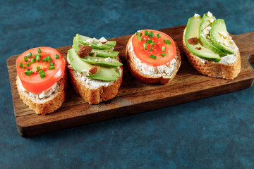 Assorted vegan bruschette snack on a wooden chopping board on a dark blue textured table. Mini sandwich mix. Top view, close up