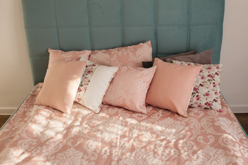 Different pillows on the bed. Close-up pink bedding sheets and pillow on light wall room background. Closeup of new bed comforter with decorative pillows. 