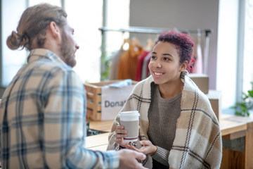 Young girl with coffee sitting and looking at talking man.