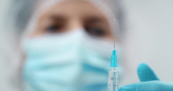 Doctor in protective uniform preparing vaccine injection, syringe closeup