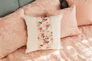 Different pillows on the bed. Close-up pink bedding sheets and pillow on light wall room background. Closeup of new bed comforter with decorative pillows. 