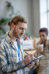 Young focused man with a badge standing and writing.
