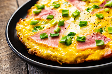 Breakfast - scrambled eggs with ham and vegetables on wooden background