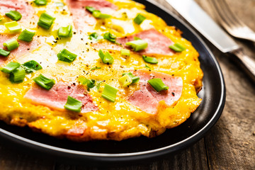 Breakfast - scrambled eggs with ham and vegetables on wooden background