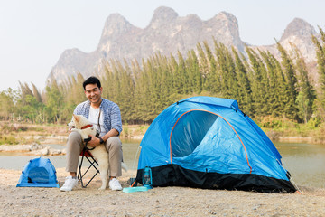 Asian young man in blue shirt with cute puppy dog camping on the lake hill mountain view happy and enjoy life