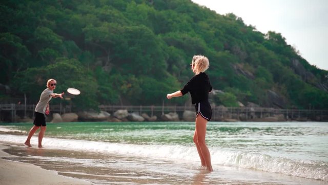 Slow-motion footage of two young women throwing a frisbee at the tropical beach on a sunny day.