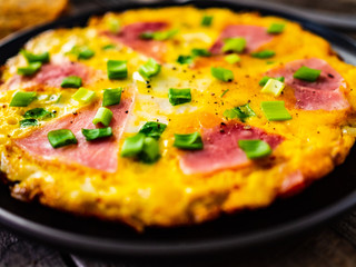 Breakfast - scrambled eggs with ham and vegetables on wooden background